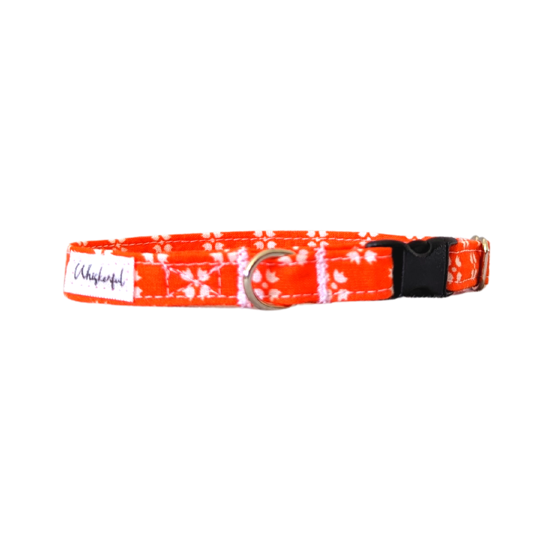  Image of our Small Bright Orange with White FloralCollar featuring a black buckle with an aluminum slider and an aluminum D-ring. The collar is designed with both a breakaway buckle option for added safety and a regular buckle for those who prefer it. The hardware is contoured for comfort and provides a secure attachment point for name tags and identification for pets.